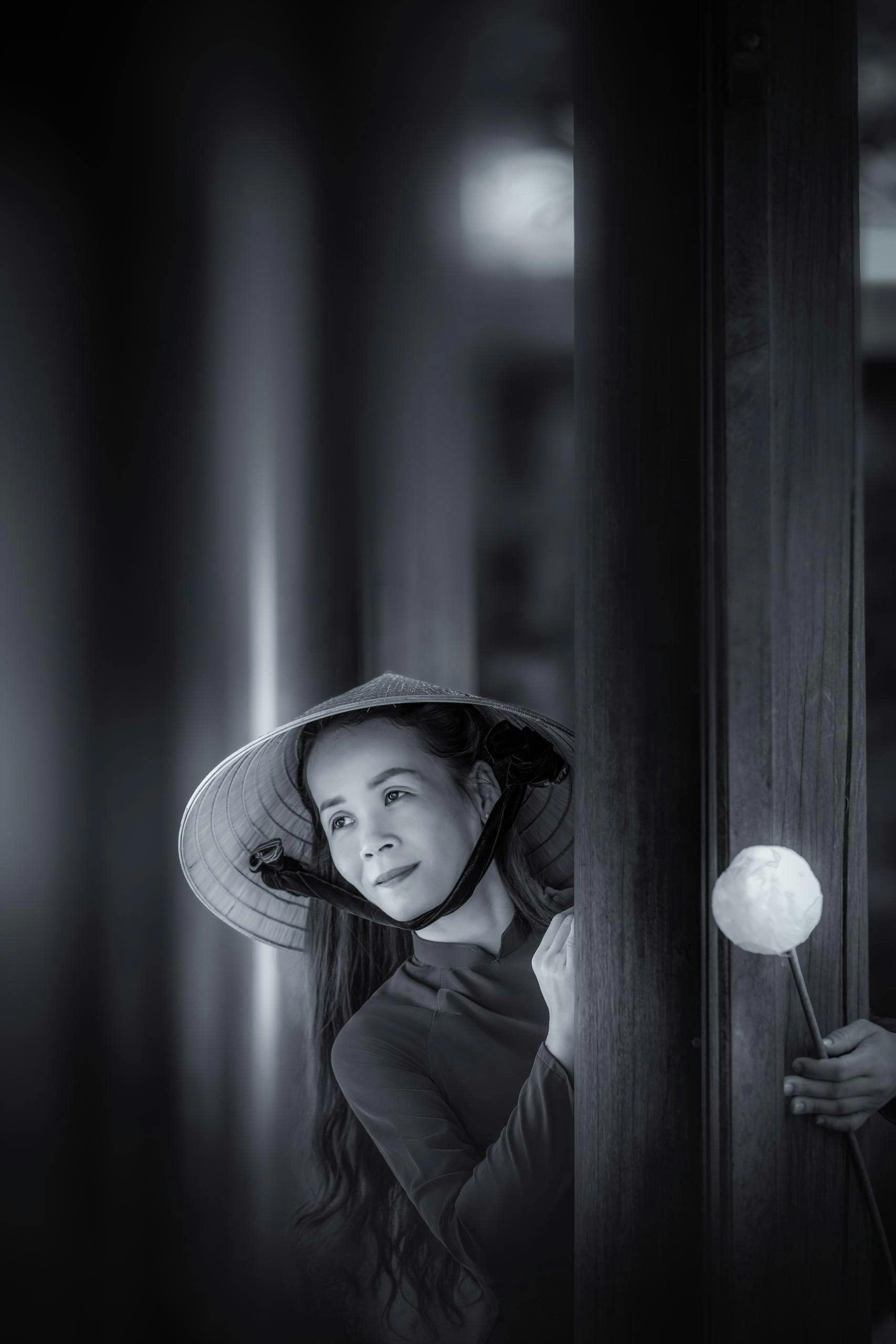 бесплатная Элегантный портрет вьетнамской женщины, выглядывающей из-за колонны в конической шляпе. Стоковое фото