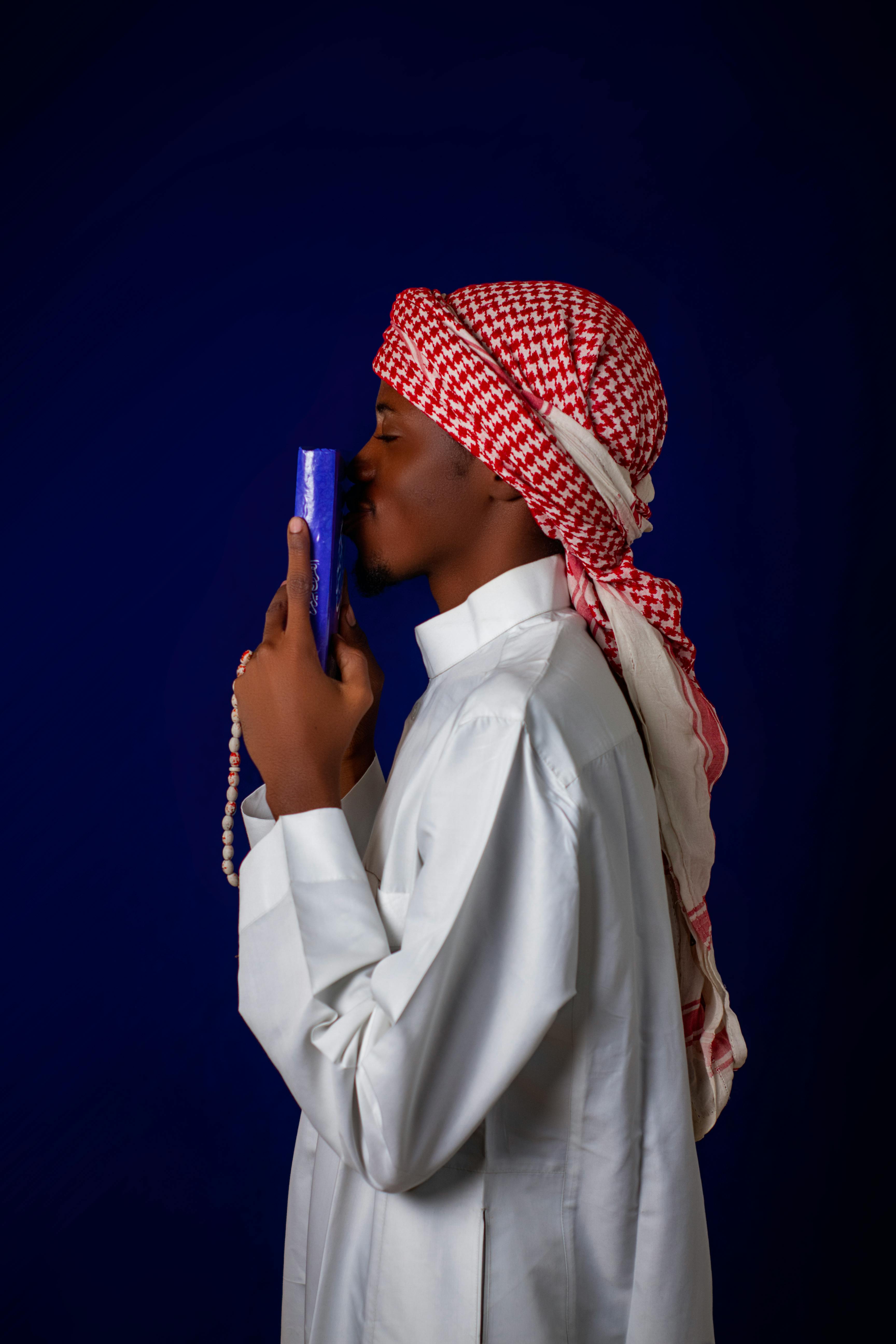 gratis Zijprofiel van een man in traditionele kleding die een boek kust, tegen een donkerblauwe achtergrond. Stockfoto