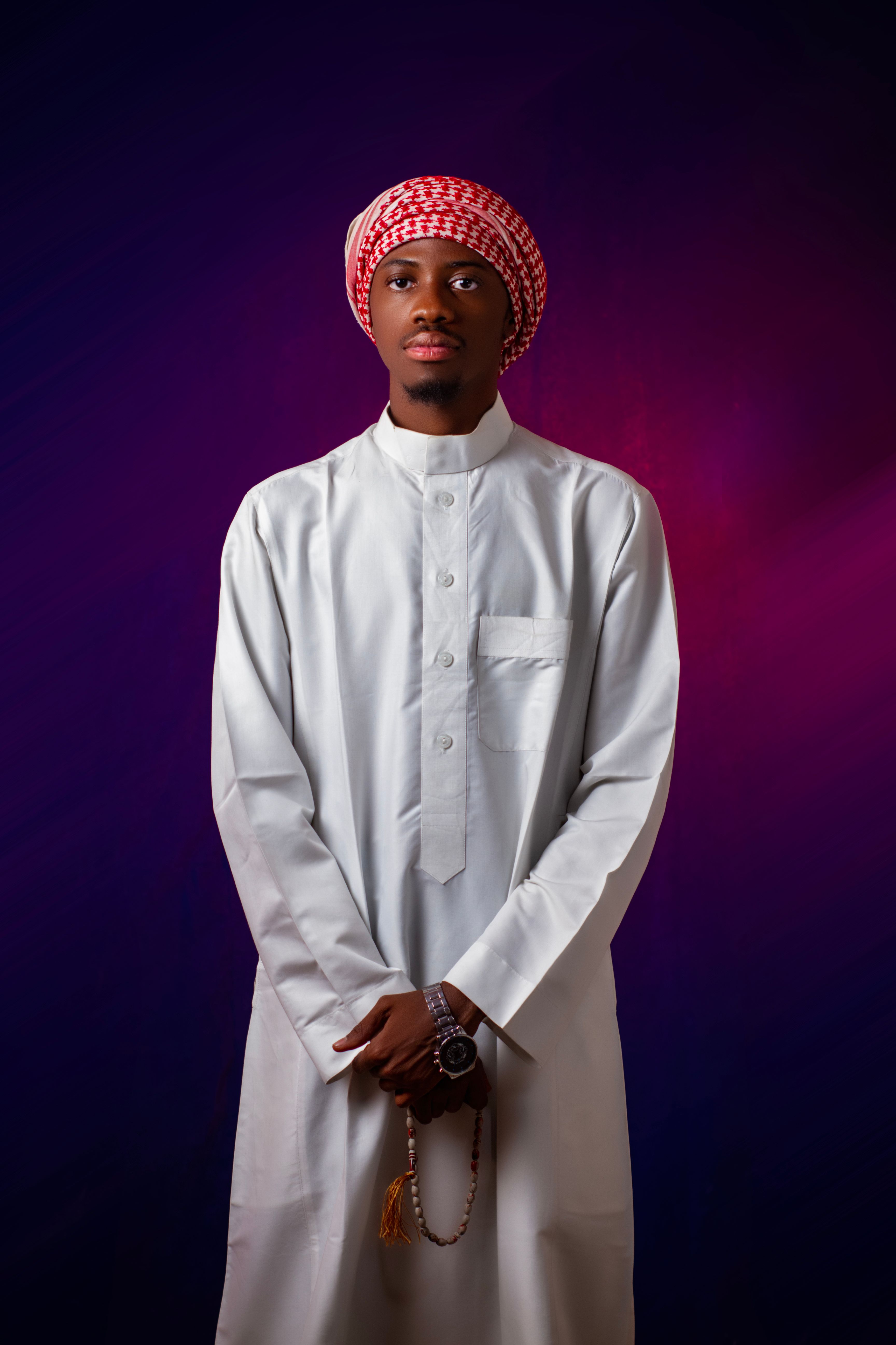 A man in traditional Middle Eastern attire with a red keffiyeh stands against a vibrant background.