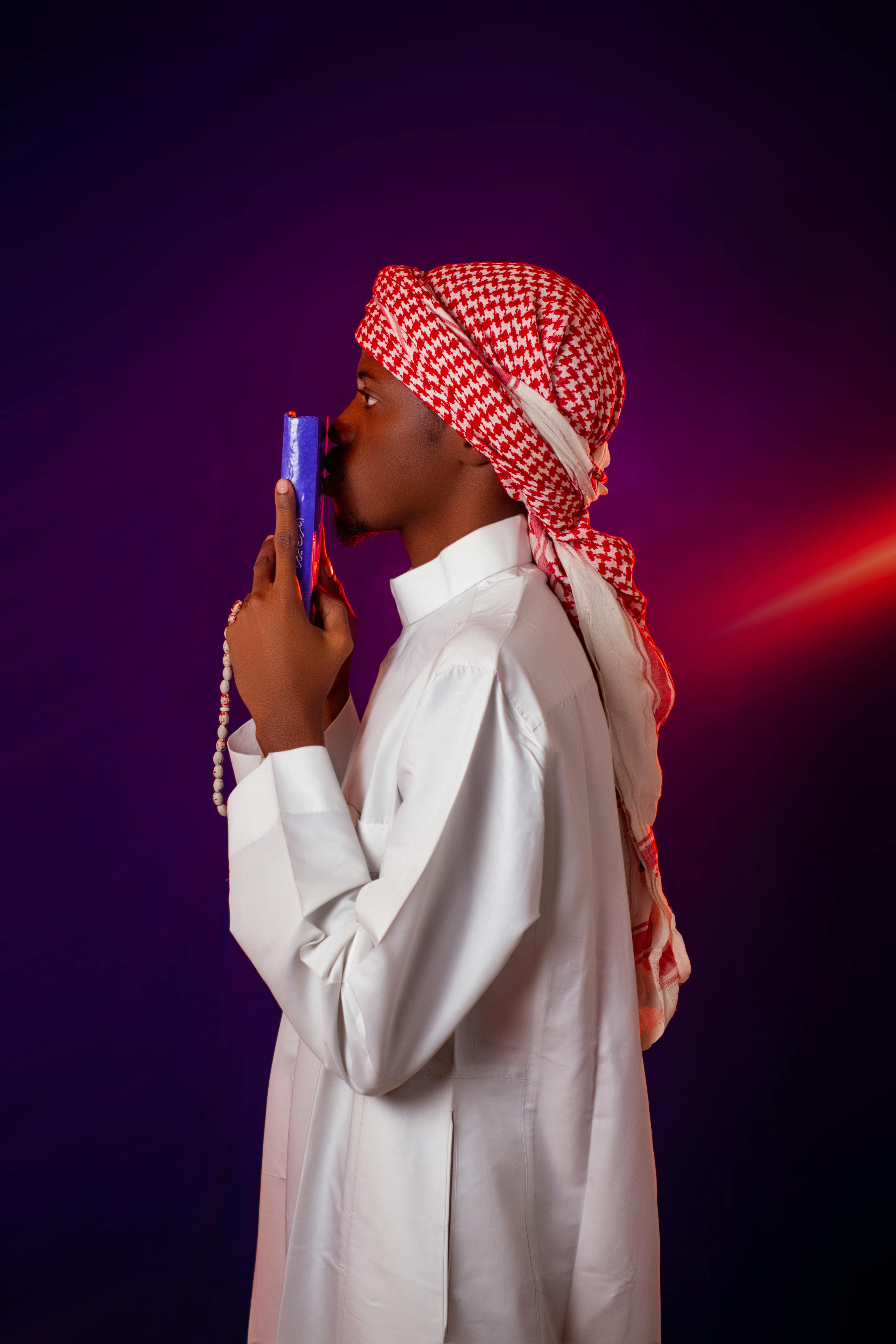 Kostenlos Seitenansicht eines Mannes in traditioneller Kleidung, der einen Koran hält und andächtig betet. Stock-Foto