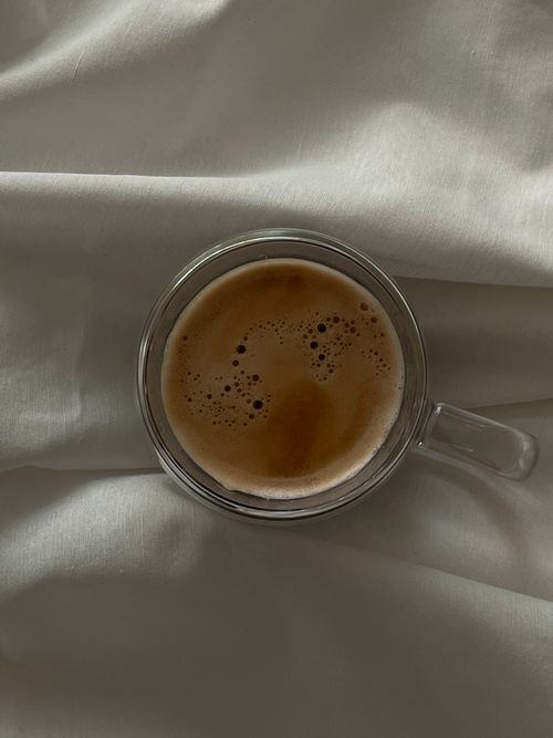 Free A soothing aerial shot of a fresh espresso with crema in a clear glass cup resting on smooth white fabric. Stock Photo