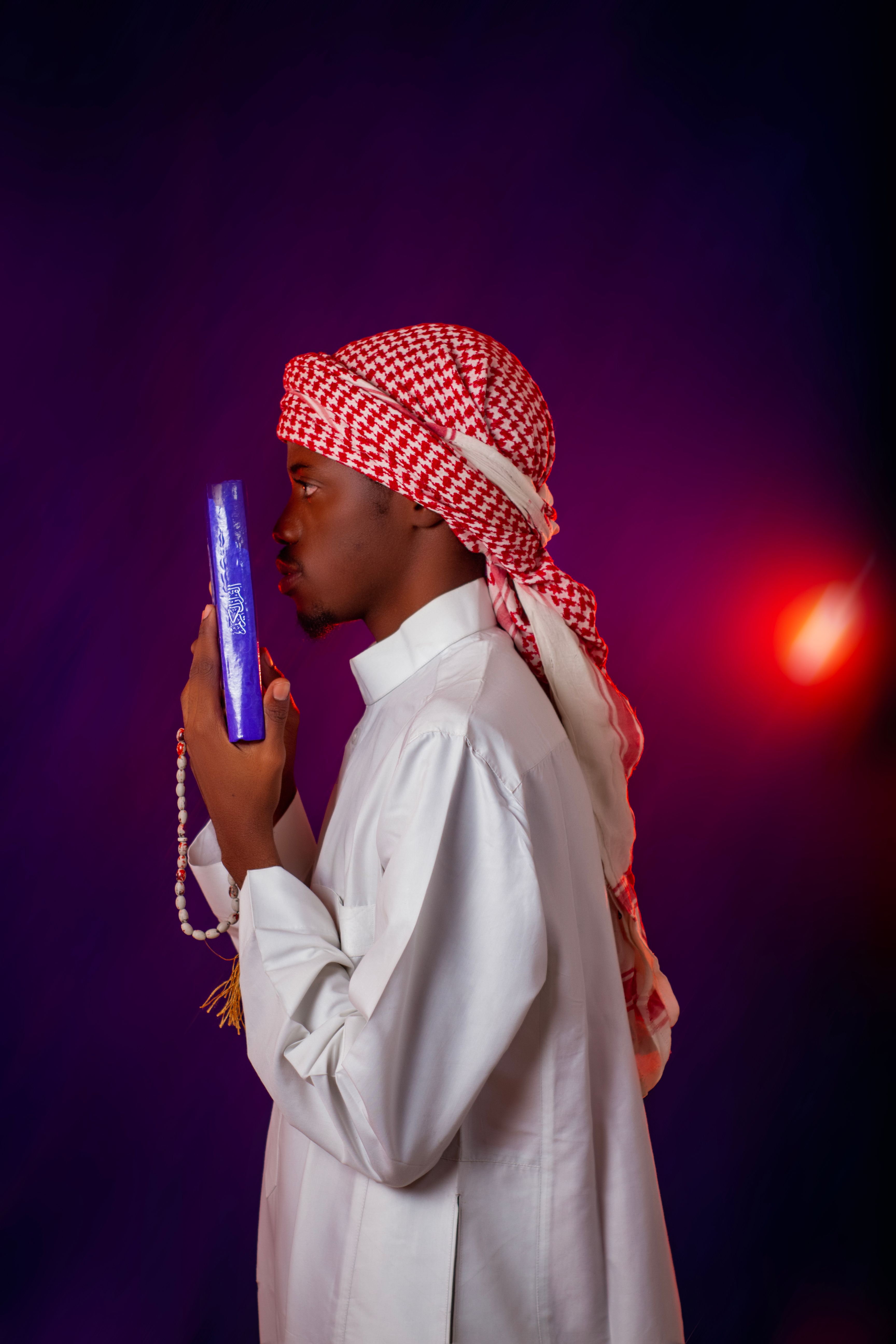 Side view of a young man in traditional attire engaging in prayer with a religious book.