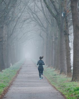 A lone runner on a foggy tree-lined path, embracing nature and solitude.