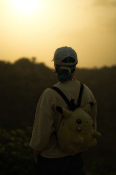A person with a Pikachu backpack gazes at the sunset, creating a serene silhouette.