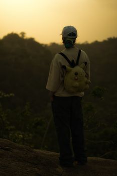 A child with a distinctive backpack gazes at the scenic landscape during sunset, creating a serene atmosphere.