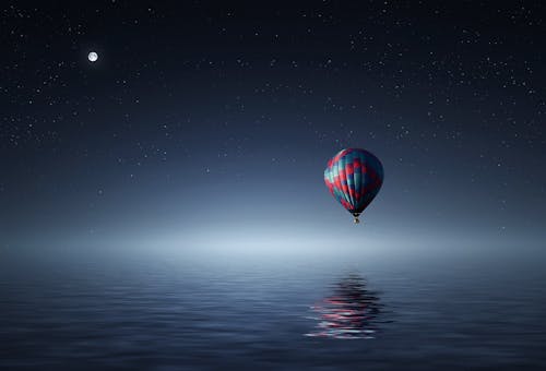 Red and Blue Hot Air Balloon Floating on Air on Body of Water during Night Time