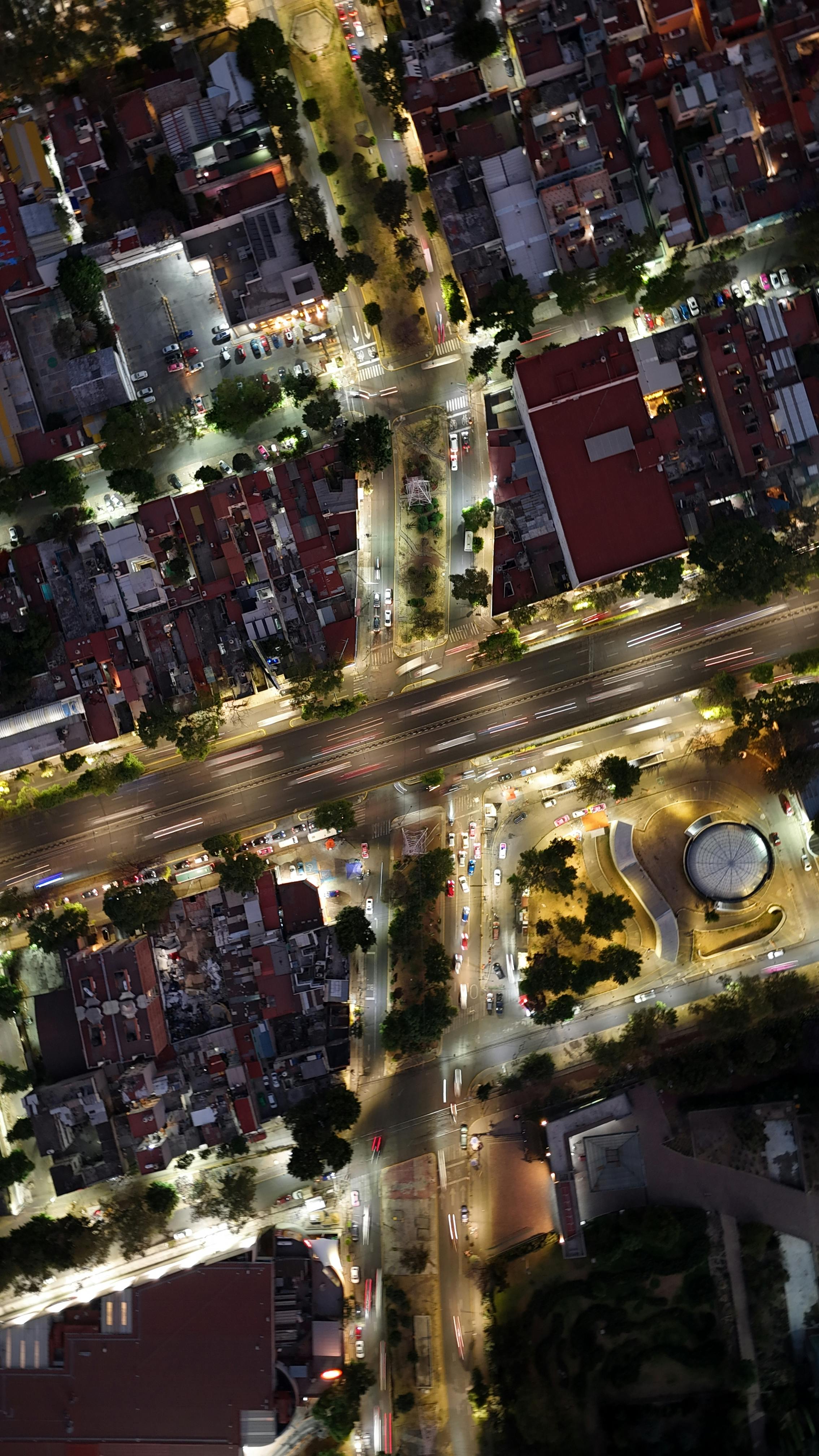 Aerial photograph of a brightly lit intersection in a city, displaying vibrant streets and buildings at night.