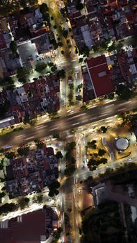 Aerial photograph of a brightly lit intersection in a city, displaying vibrant streets and buildings at night.
