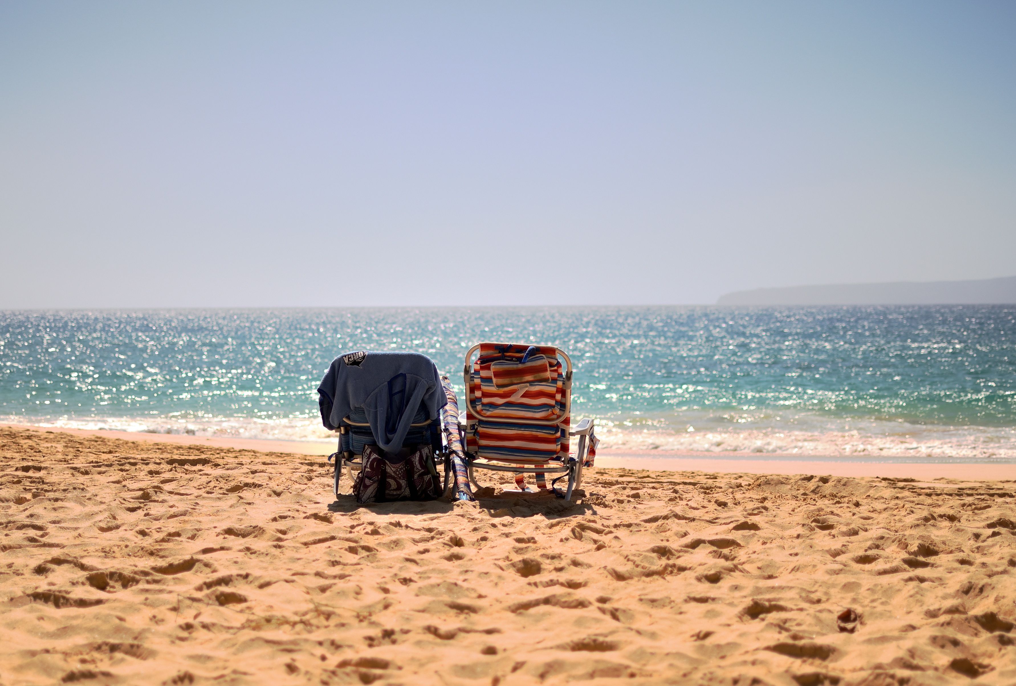 Two beach chairs facing the ocean on a sunny Hawaiian beach, perfect for relaxation.