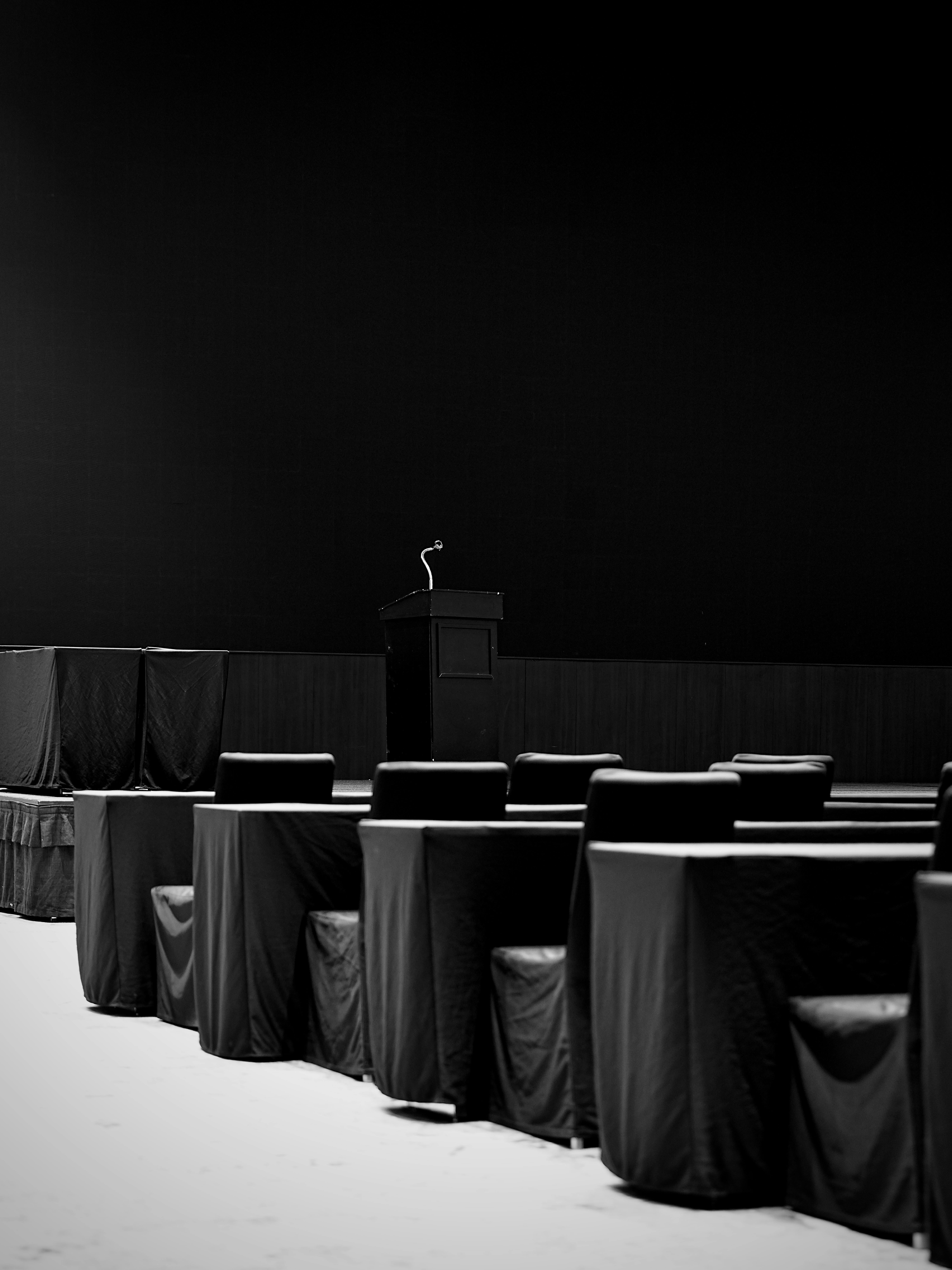 無料 演台と椅子が置かれた空の会議室の白黒写真。ドラマチックでエレガントな雰囲気を醸し出しています。 写真素材