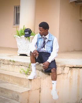 Young man in denim vest sitting on steps outdoors. Urban fashion style.