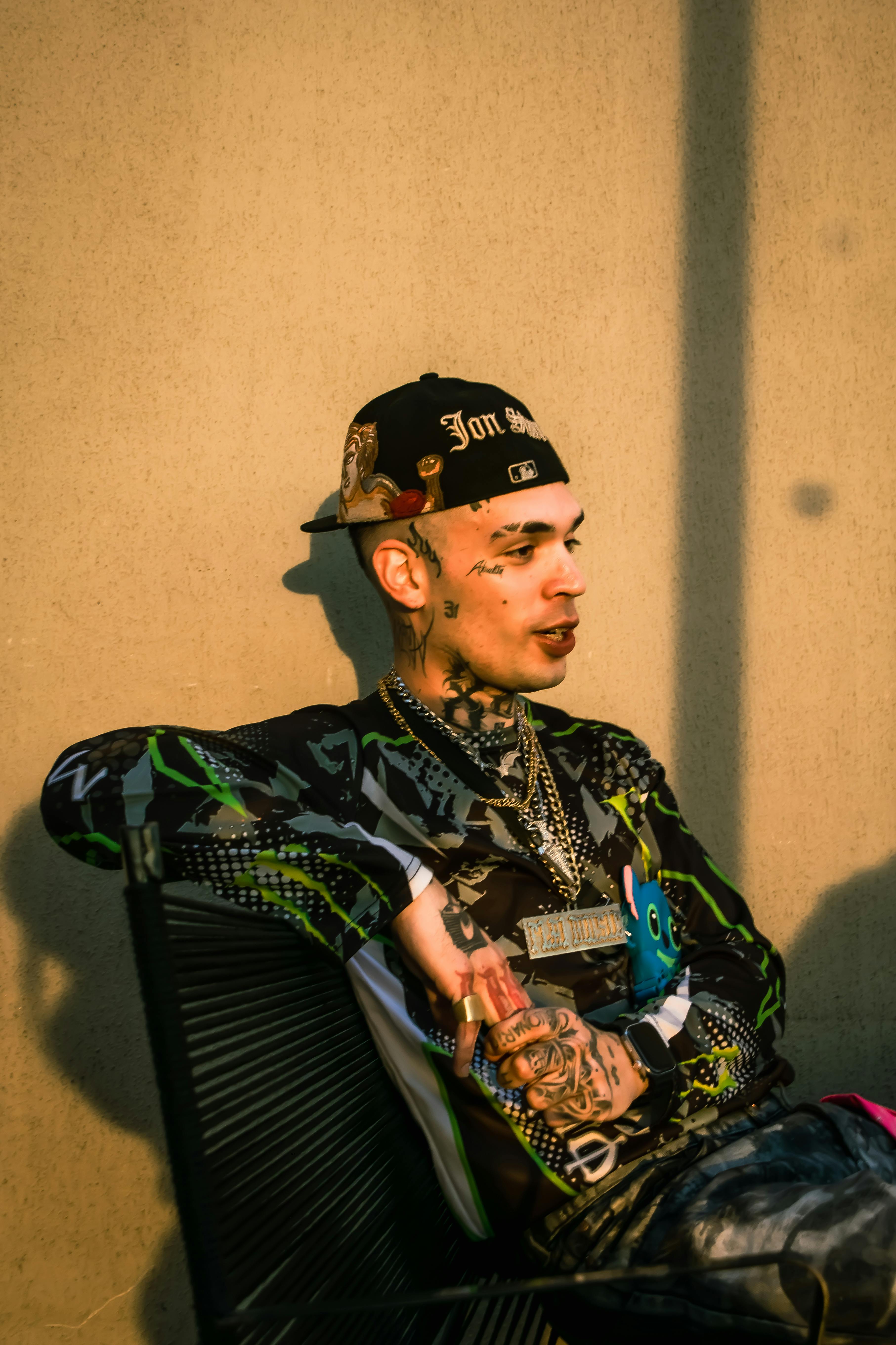 Young tattooed man in urban outfit sitting outdoors in evening sun.