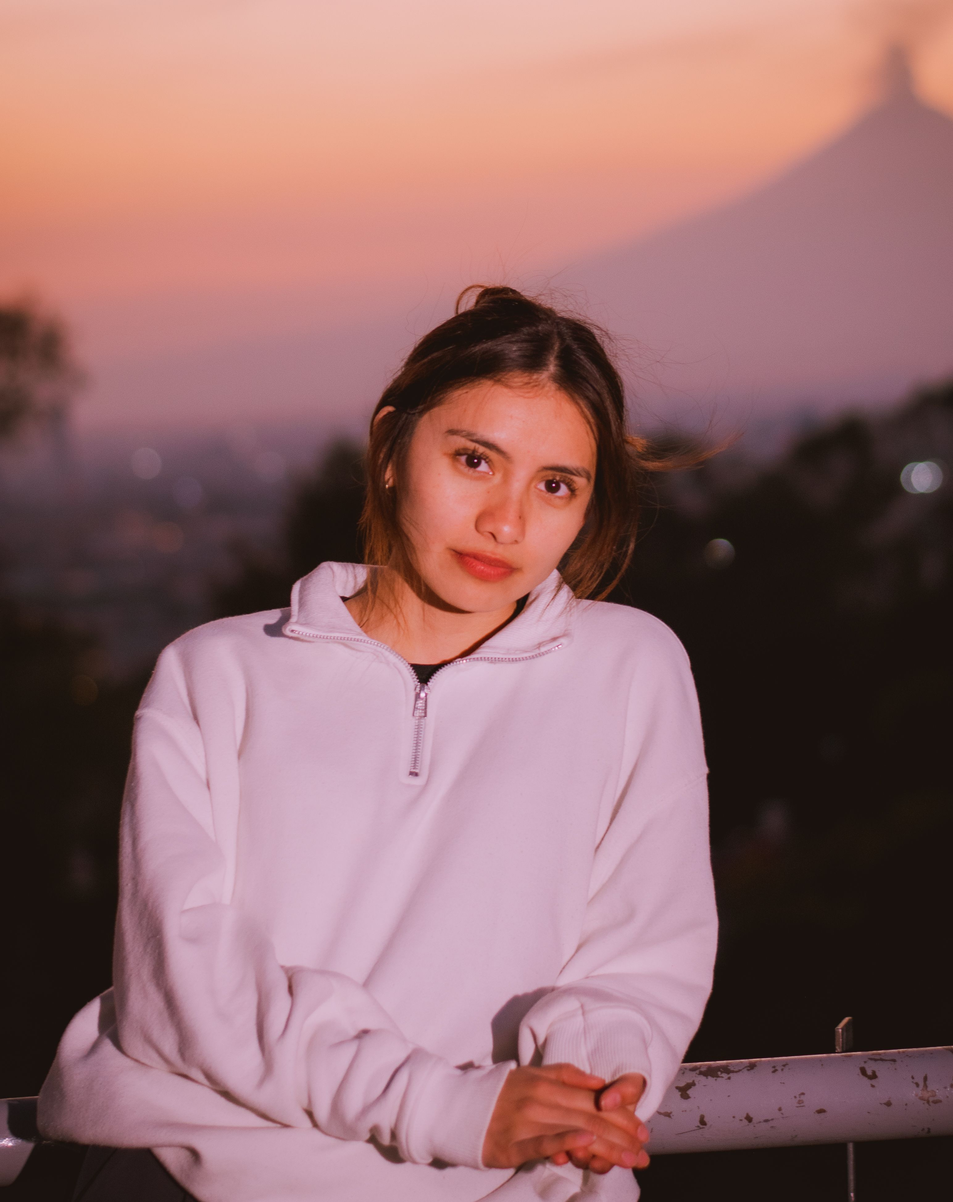 Portrait of a young woman at twilight with a scenic sunset backdrop and silhouetted mountain.