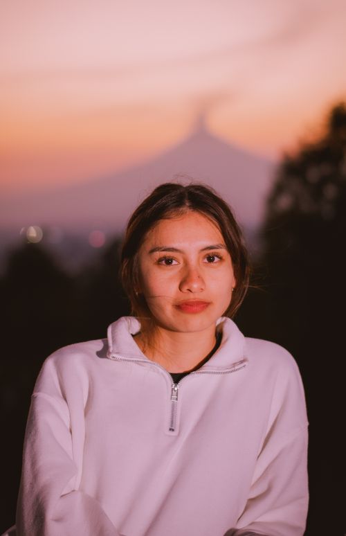 Free Young woman in a white sweatshirt poses outdoors at dusk with a mountain silhouette in the background. Stock Photo
