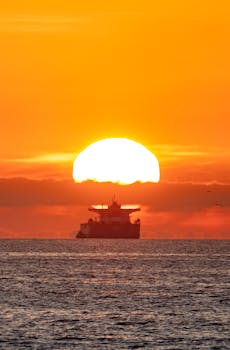 Photo by Soly Moses Oil tanker silhouette against a vibrant sunset over the Pacific Ocean, creating a stunning seascape.