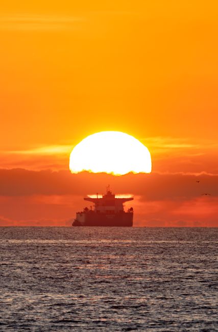 Photo by Soly Moses Oil tanker silhouette against a vibrant sunset over the Pacific Ocean, creating a stunning seascape.