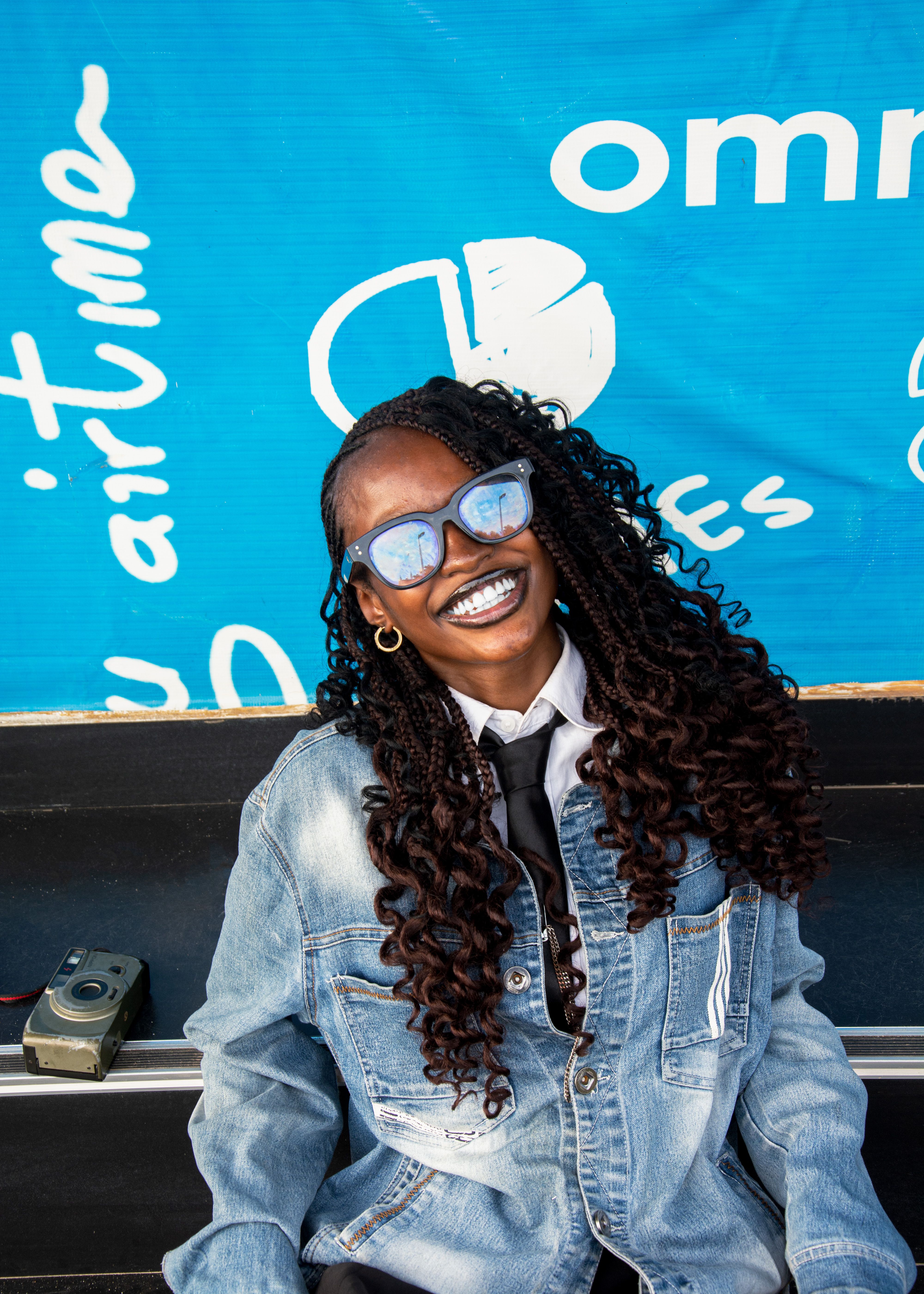 Portrait of a stylish woman in a denim jacket, smiling brightly outdoors.