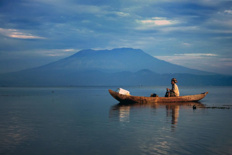 Serene scene of a person in a canoe on a calm lake with mountains in West Sumatra, Indonesia.