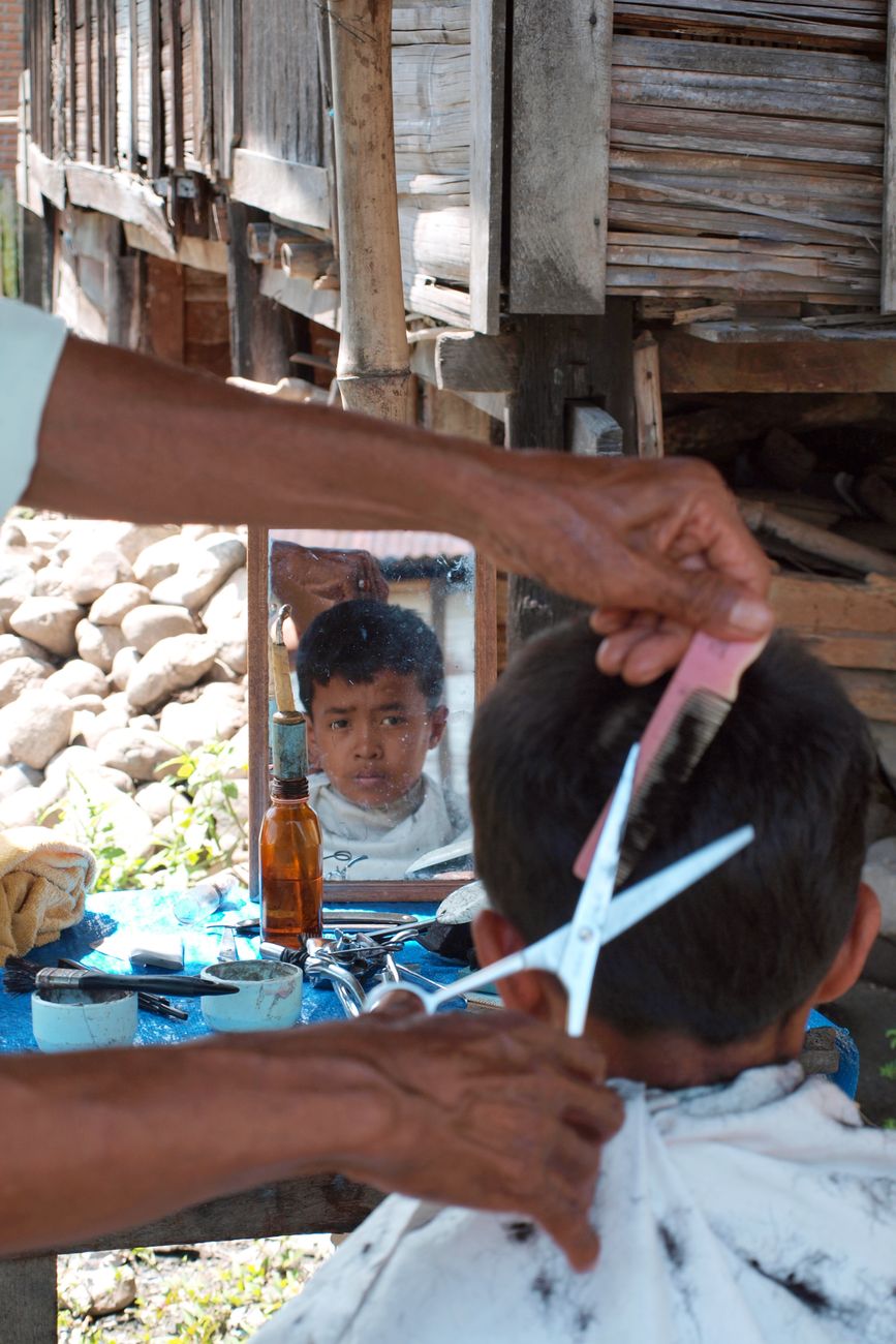 Een kind krijgt een knipbeurt in de buitenlucht in een landelijk Indonesisch dorp.
