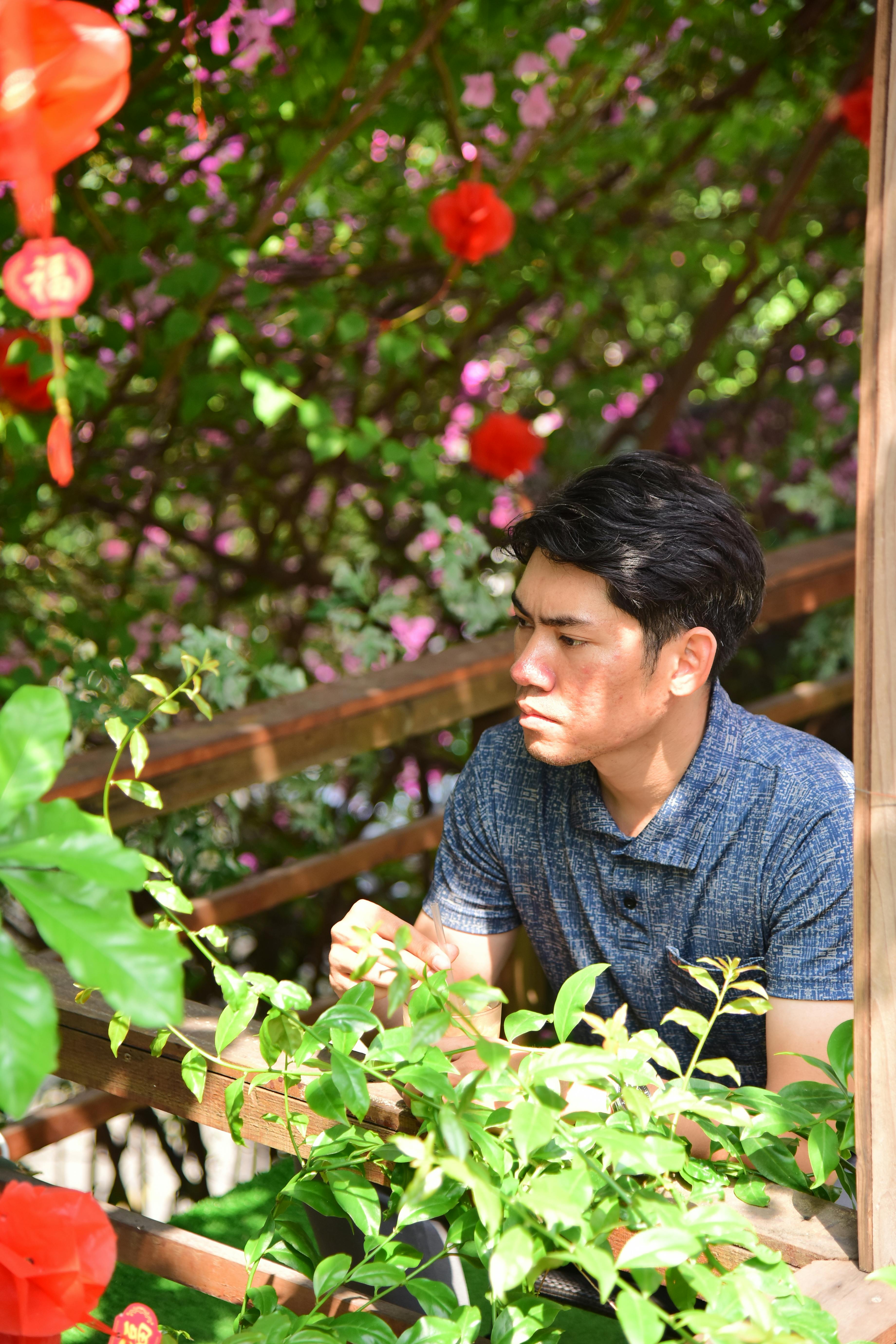 Free A young man sits thoughtfully amidst a vibrant garden with red lanterns and greenery. Stock Photo