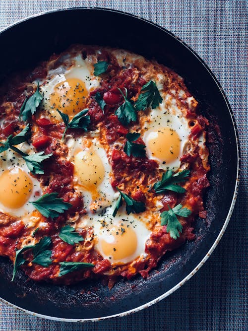Free Top view of delicious breakfast consisting of fried eggs with tomato sauce and parsley in pan on table Stock Photo