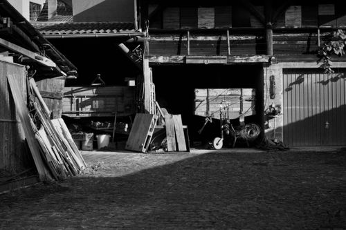 Free A black and white photo capturing a rustic barn yard with old wooden structures and shadows. Stock Photo