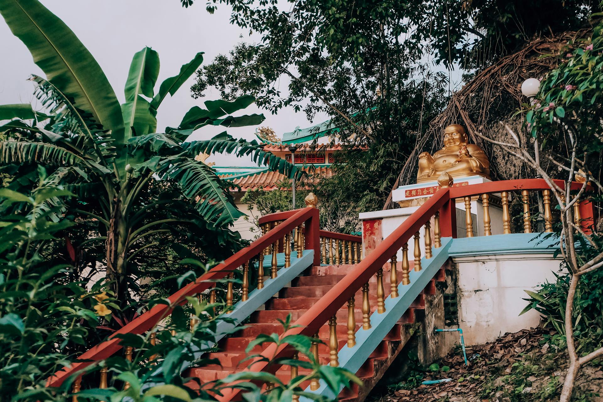 Aged golden statuette of god placed on top of red stairs in traditional oriental temple in garden