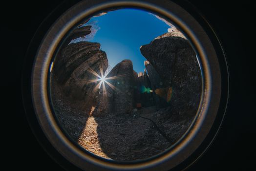 Captivating fisheye lens view of rocky landscape with sunburst, clear blue sky.