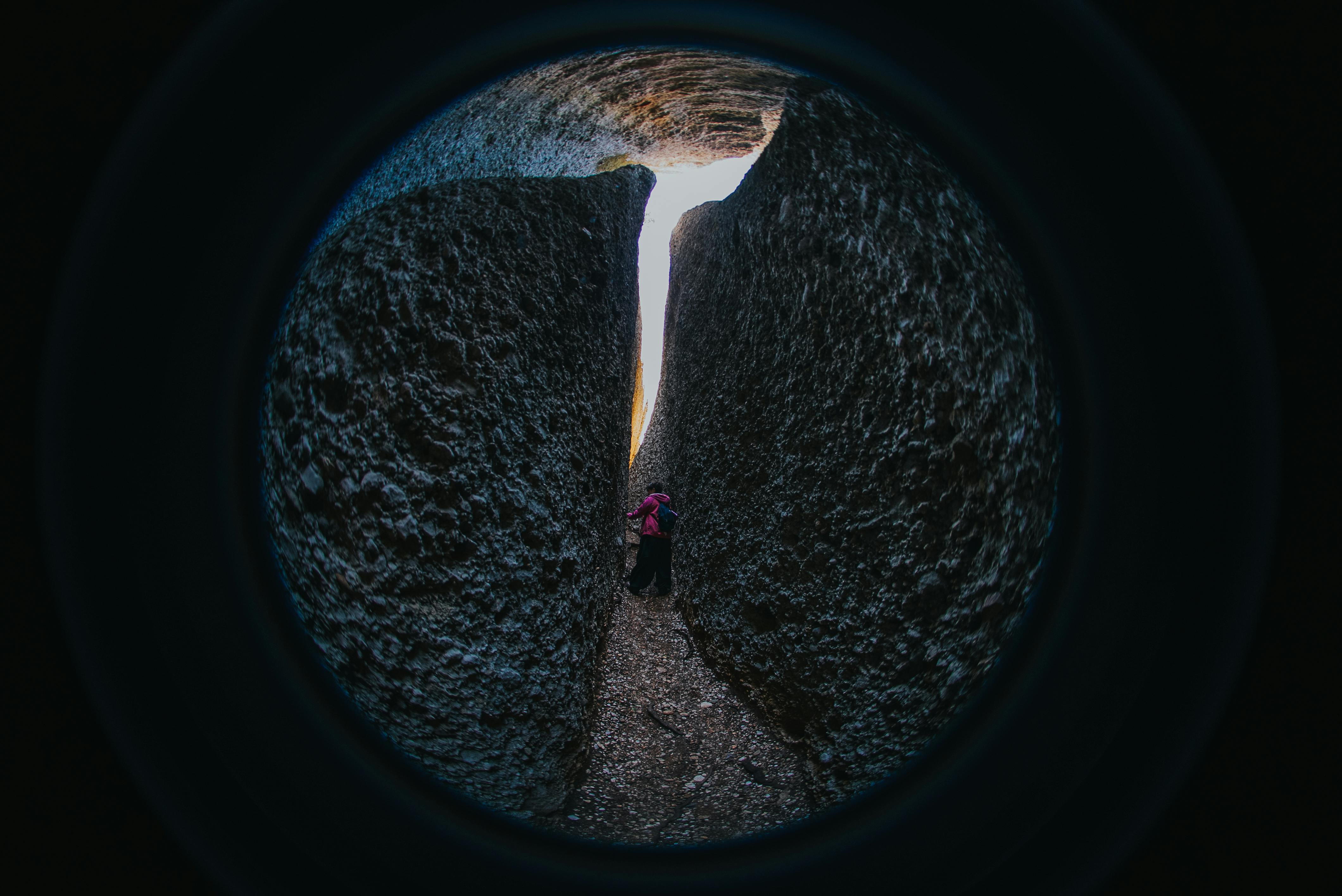 Kostnadsfria En person navigerar i en smal passage mellan stora klippformationer, fångad med ett fisheye-objektiv. Stock foto
