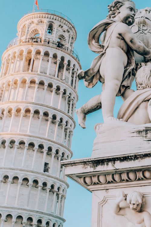 Free Leaning Tower of Pisa seen alongside an ornate cherub statue against a clear blue sky. Stock Photo