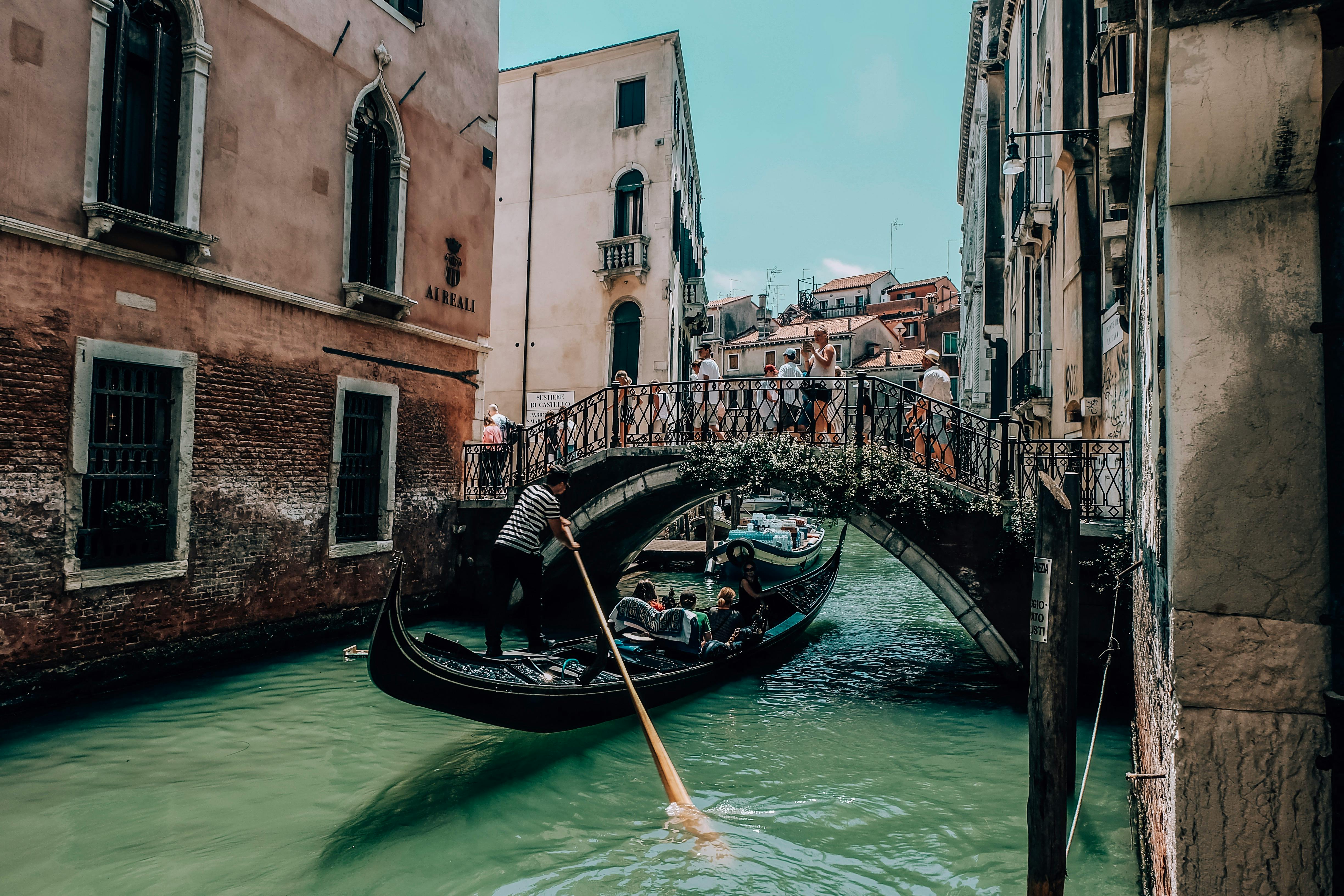 people riding a boat on river between brown concrete buildings