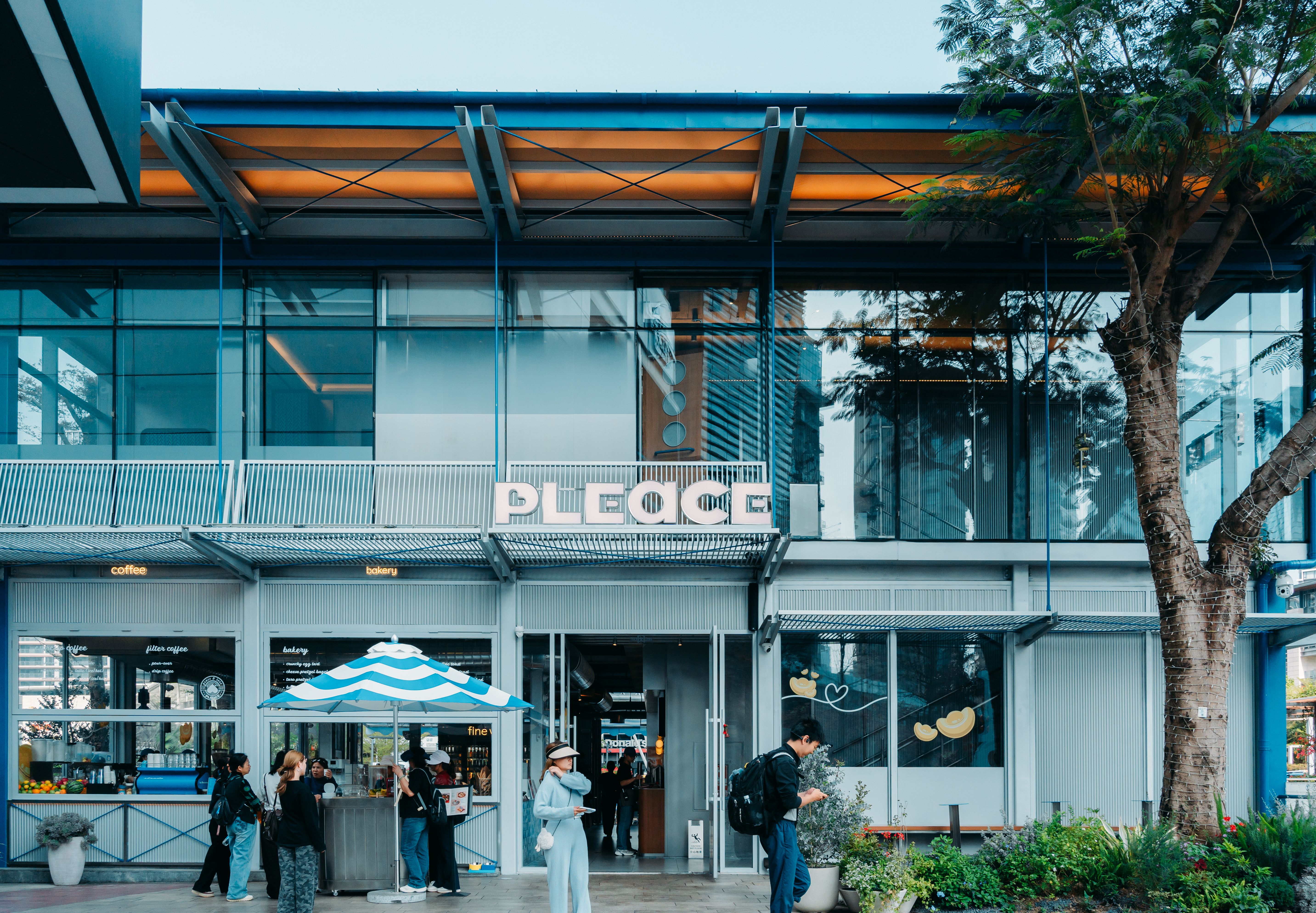 People gathering outside a modern urban cafe with glass facade and outdoor seating.