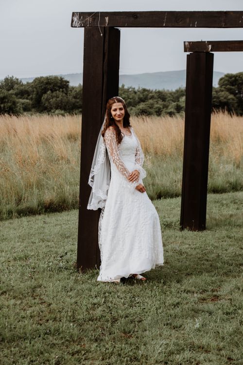 Free Beautiful bride in lace gown posing outdoors surrounded by nature, rustic wood beams creating a serene wedding scene. Stock Photo