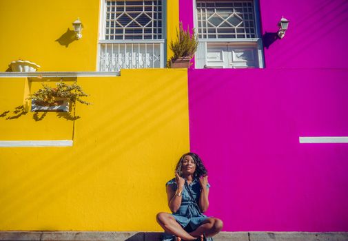 Woman sitting against a vibrant yellow and magenta wall, capturing urban color.