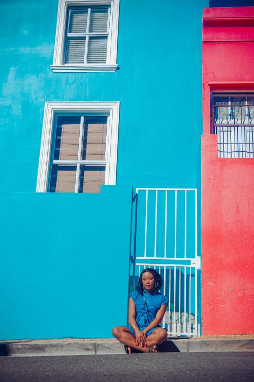 Free A woman sits against colorful walls in Bo-Kaap, Cape Town, showcasing vibrant architecture and style. Stock Photo