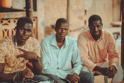 Free Three men sitting outdoors in casual clothing, posing naturally for the camera. Stock Photo