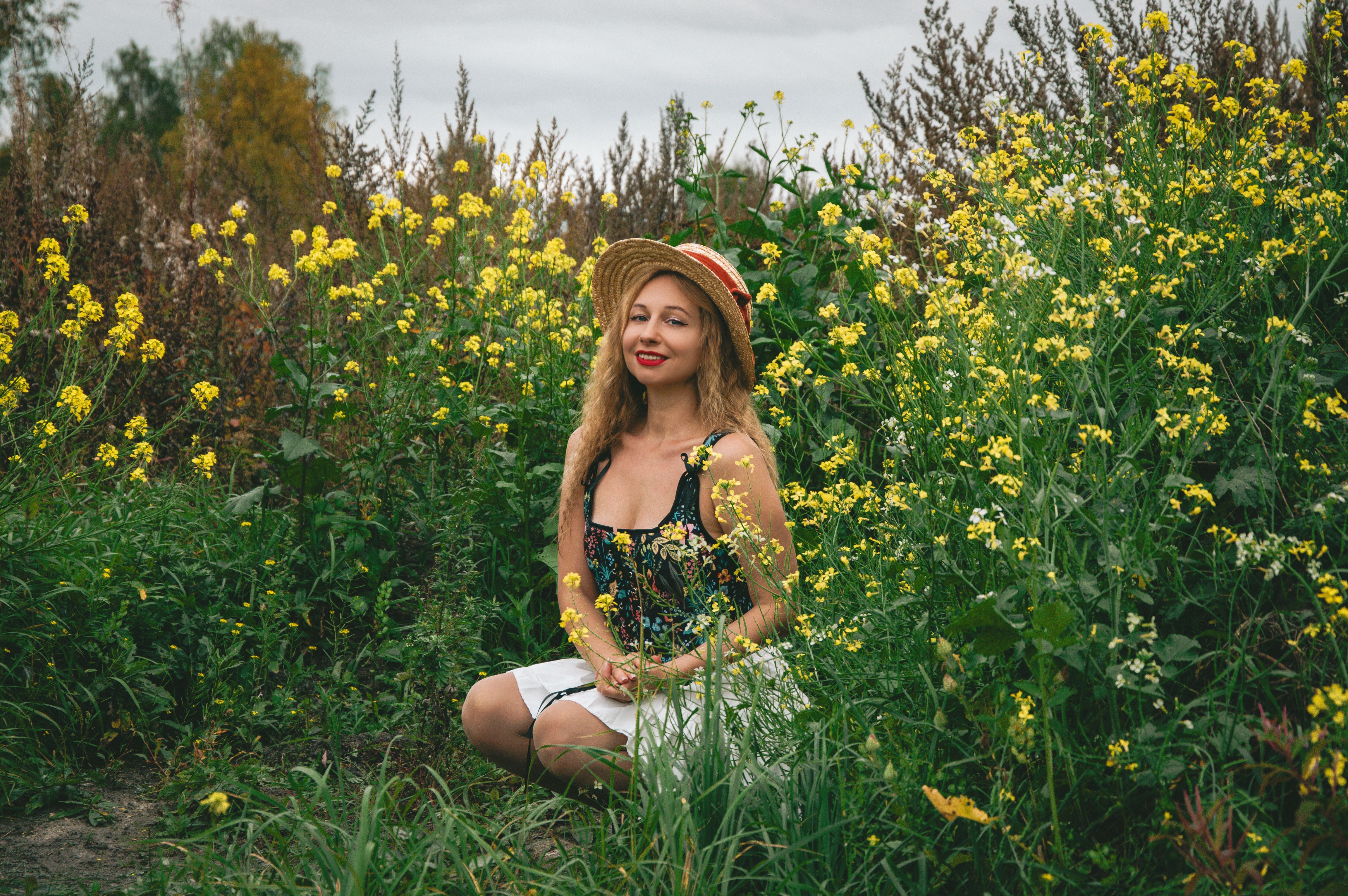 A woman in a straw hat sits amid vibrant yellow wildflowers, exuding a serene and natural vibe.
