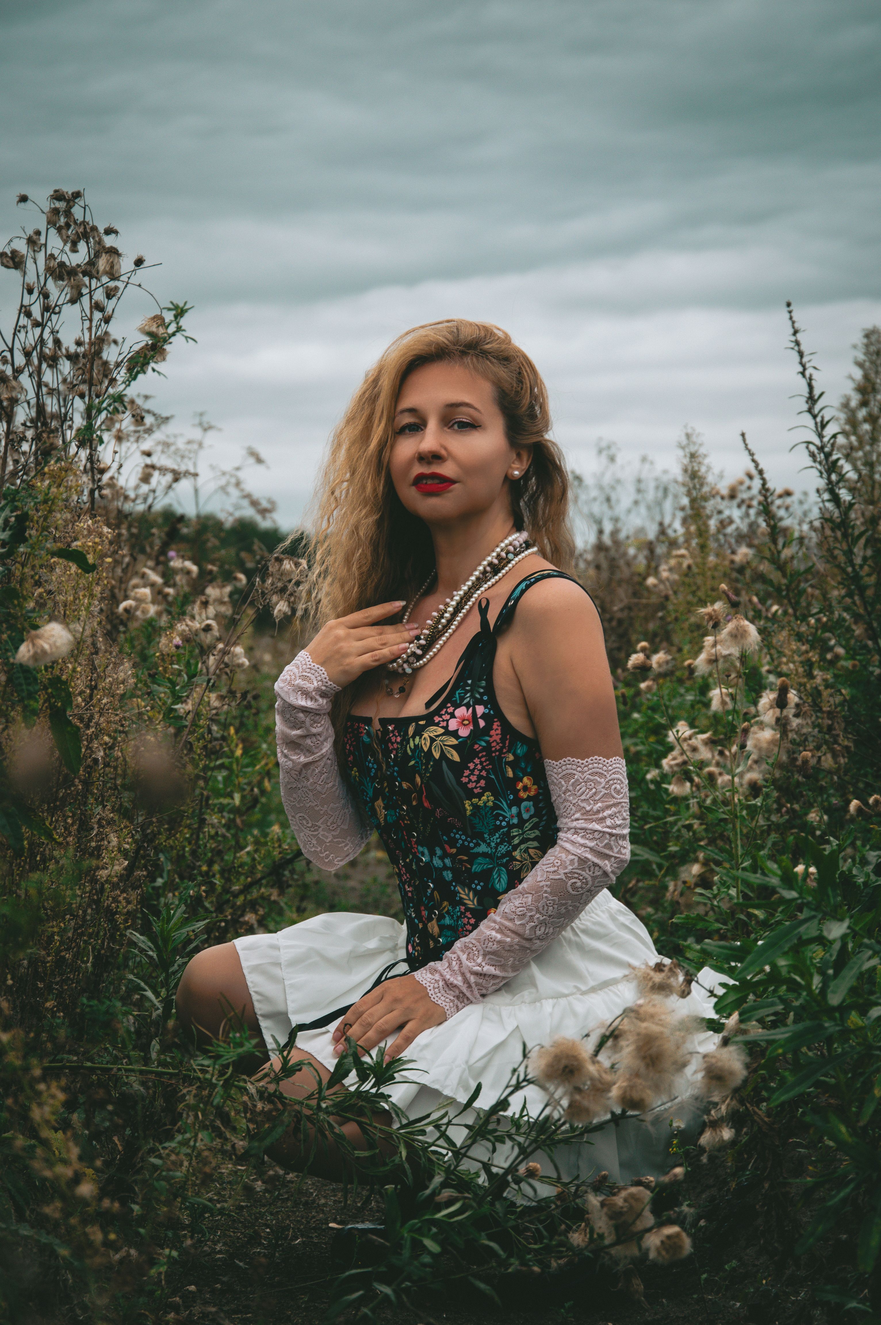 Woman in Floral Dress Sitting with Rose Outdoors · Free Stock Photo