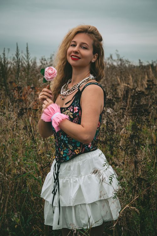 Free Smiling woman with a rose stands in a lush summer meadow wearing floral attire. Stock Photo