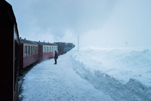 A person standing beside a steam train in a snowy winter landscape.