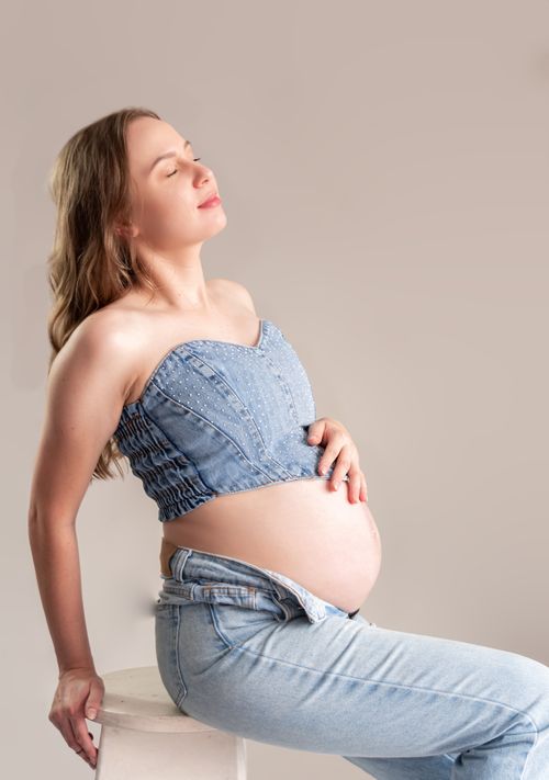 Free Pregnant woman in casual denim, seated and relaxed. Captures serenity and expectation. Stock Photo