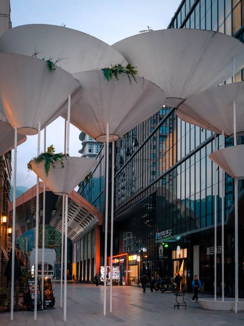 Free A cityscape featuring modern architectural umbrellas at dusk with shops and pedestrians Stock Photo