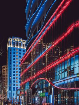 A bustling city street illuminated by vibrant neon lights on modern architecture at night.