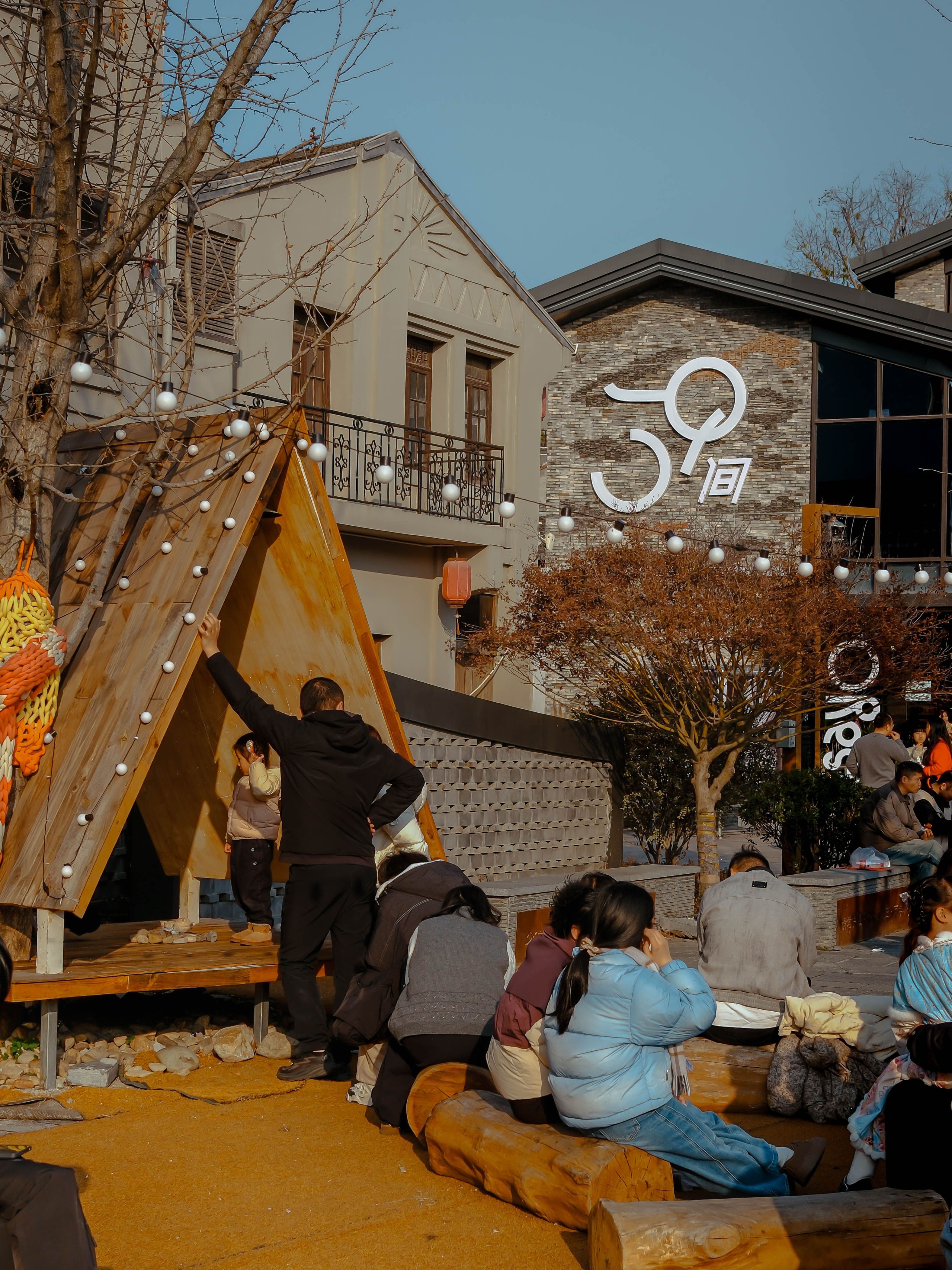 People relax outdoors at a rustic cafe with wooden seating and warm atmosphere.