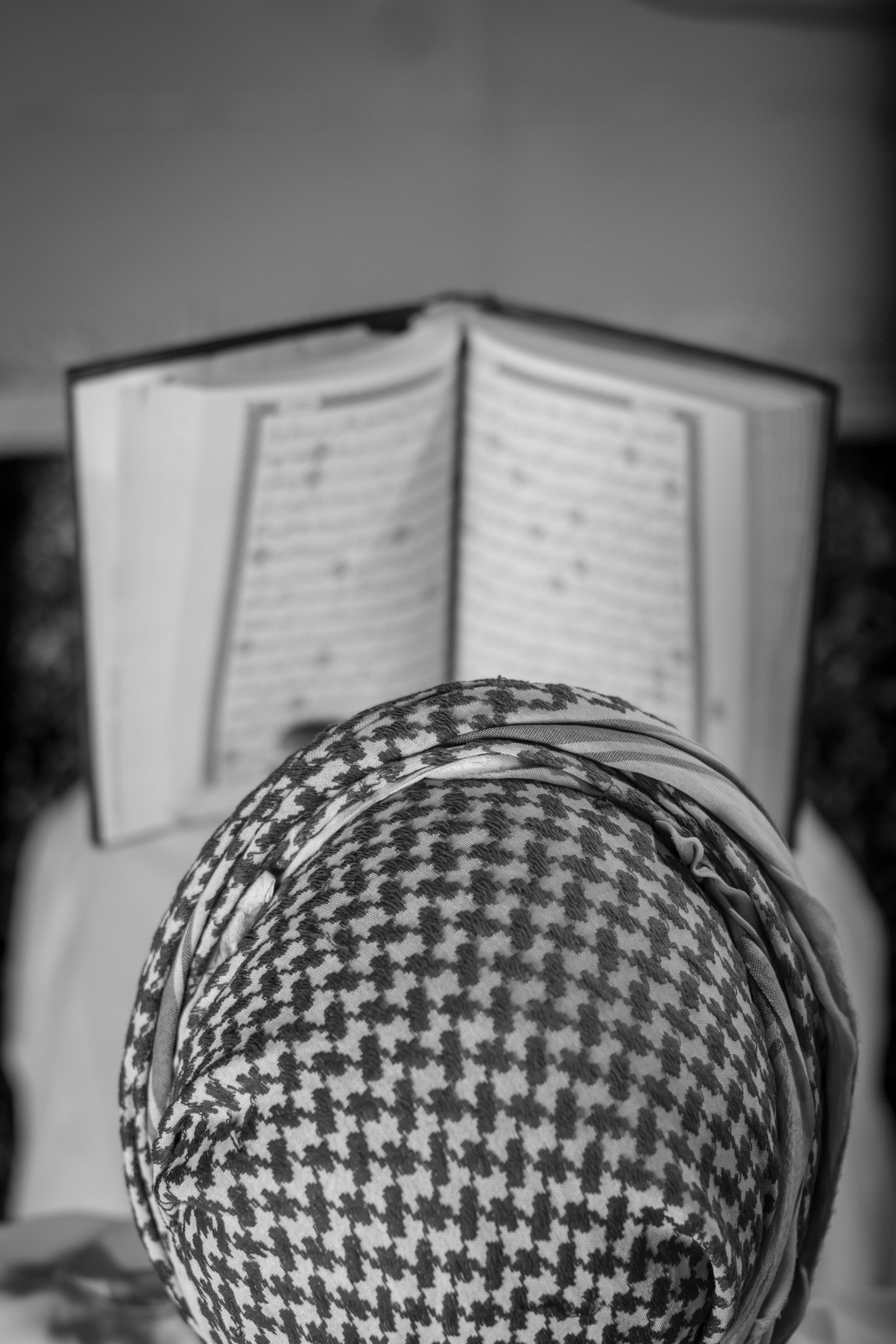 Gratis En person med et mønstret hodeskjerf leser fra en åpen religiøs tekst i gråtoner. Arkivbilde