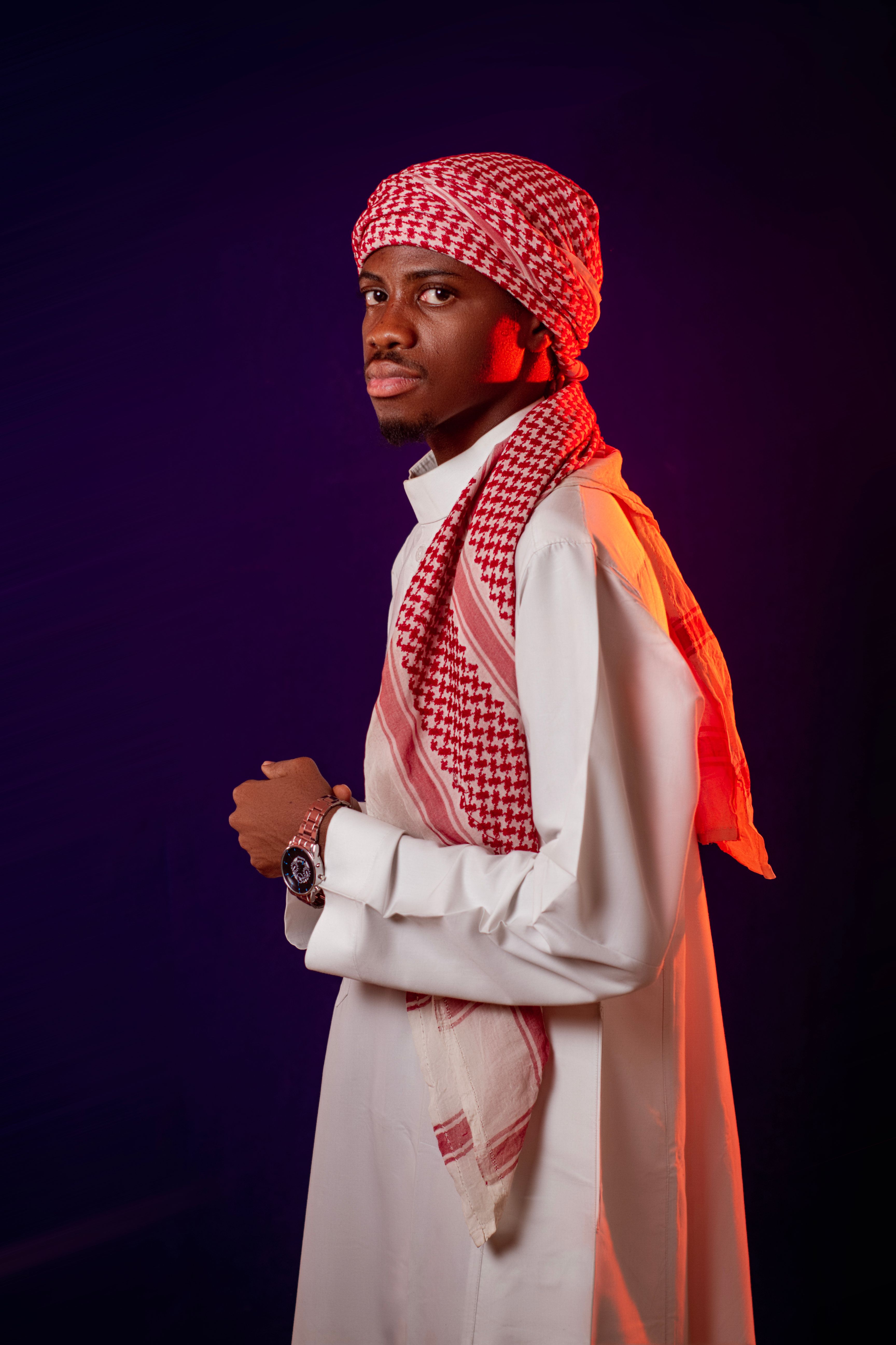 A man wearing traditional Middle Eastern attire stands against a dark background.