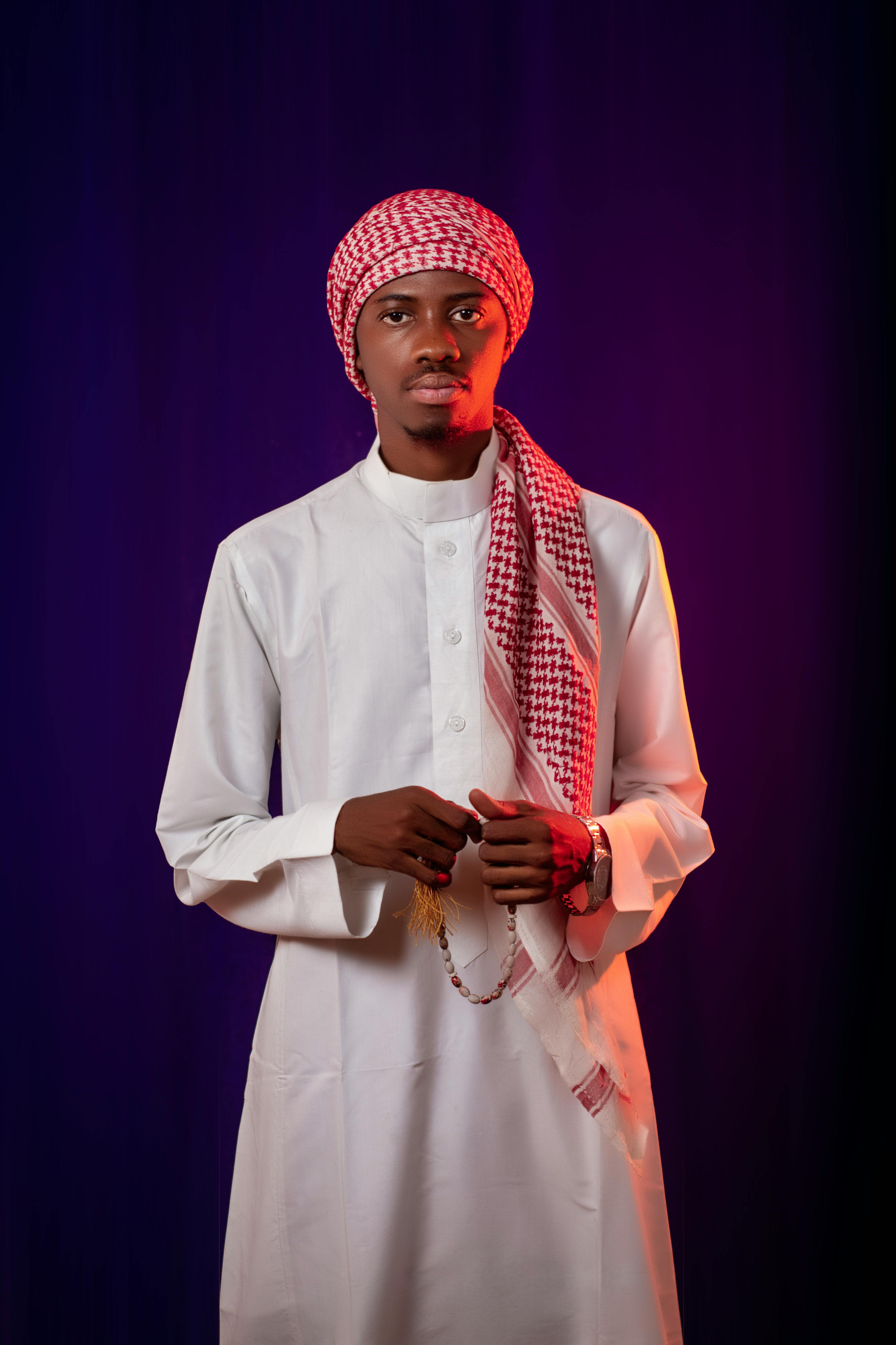 Man in traditional Middle Eastern attire with a scarf, posing against a dark backdrop.