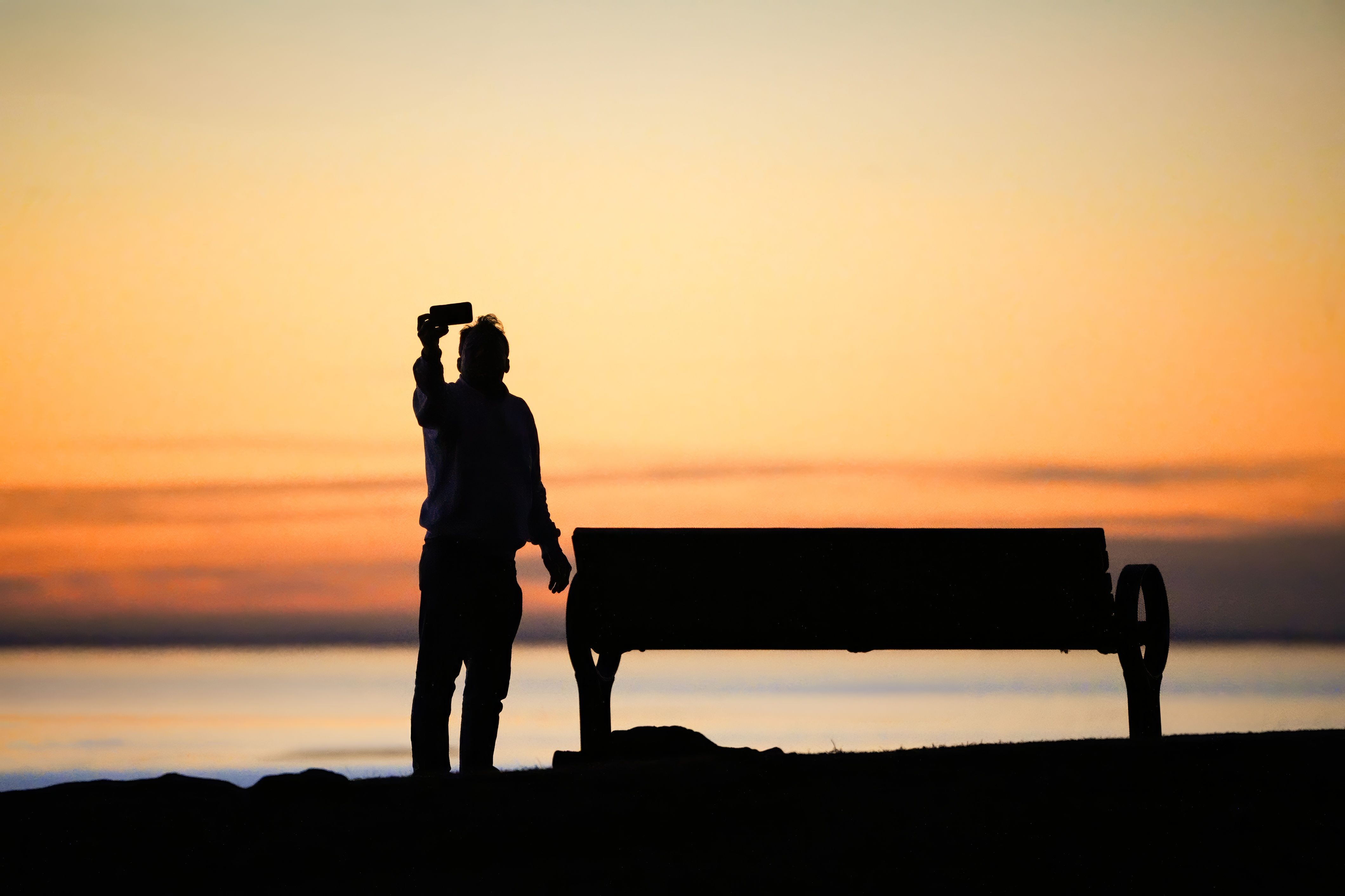 A person looking at their phone in a beautiful, peaceful natural setting, oblivious to the sunset