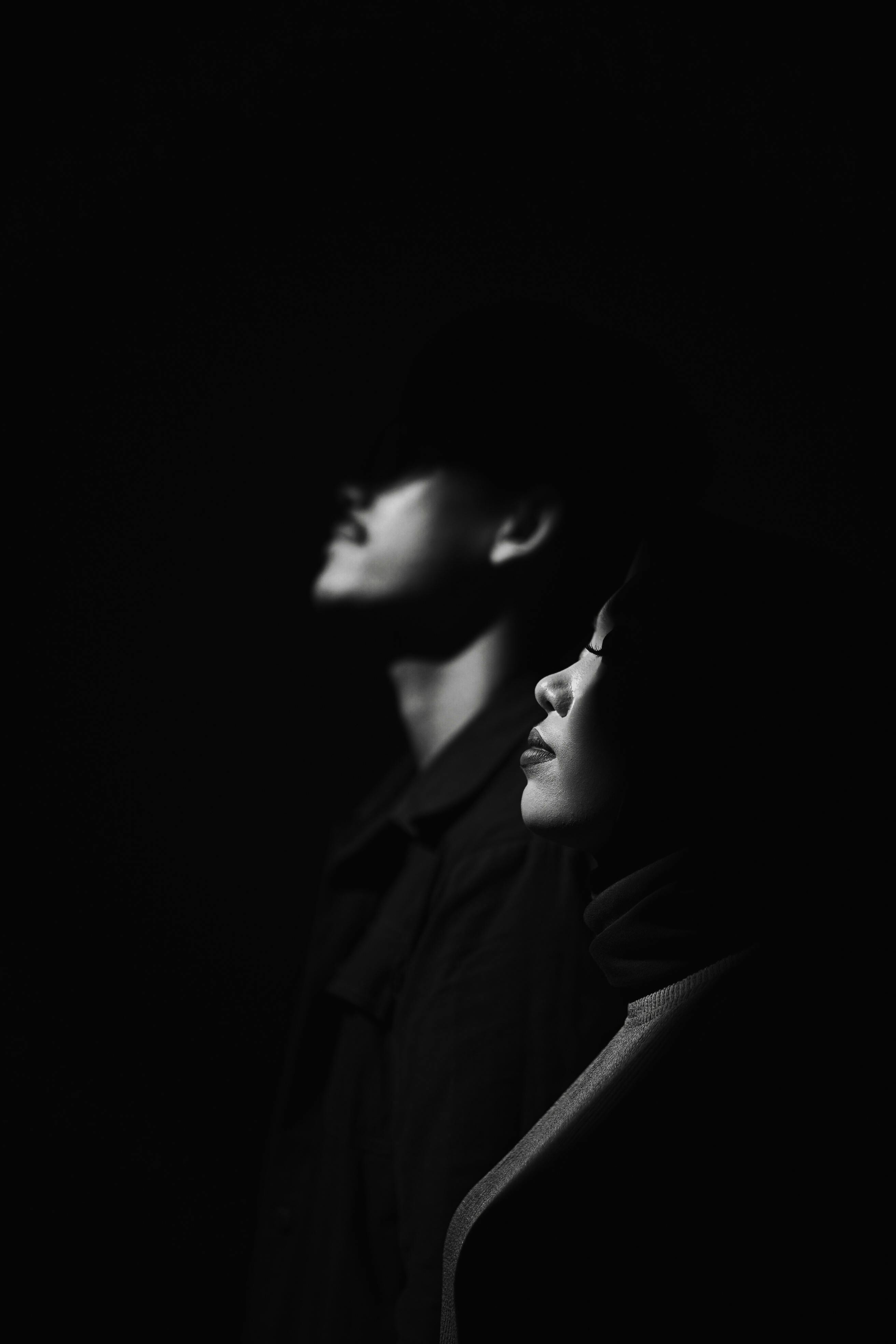 Side profile of two adults captured in dramatic lighting, evoking a moody atmosphere.