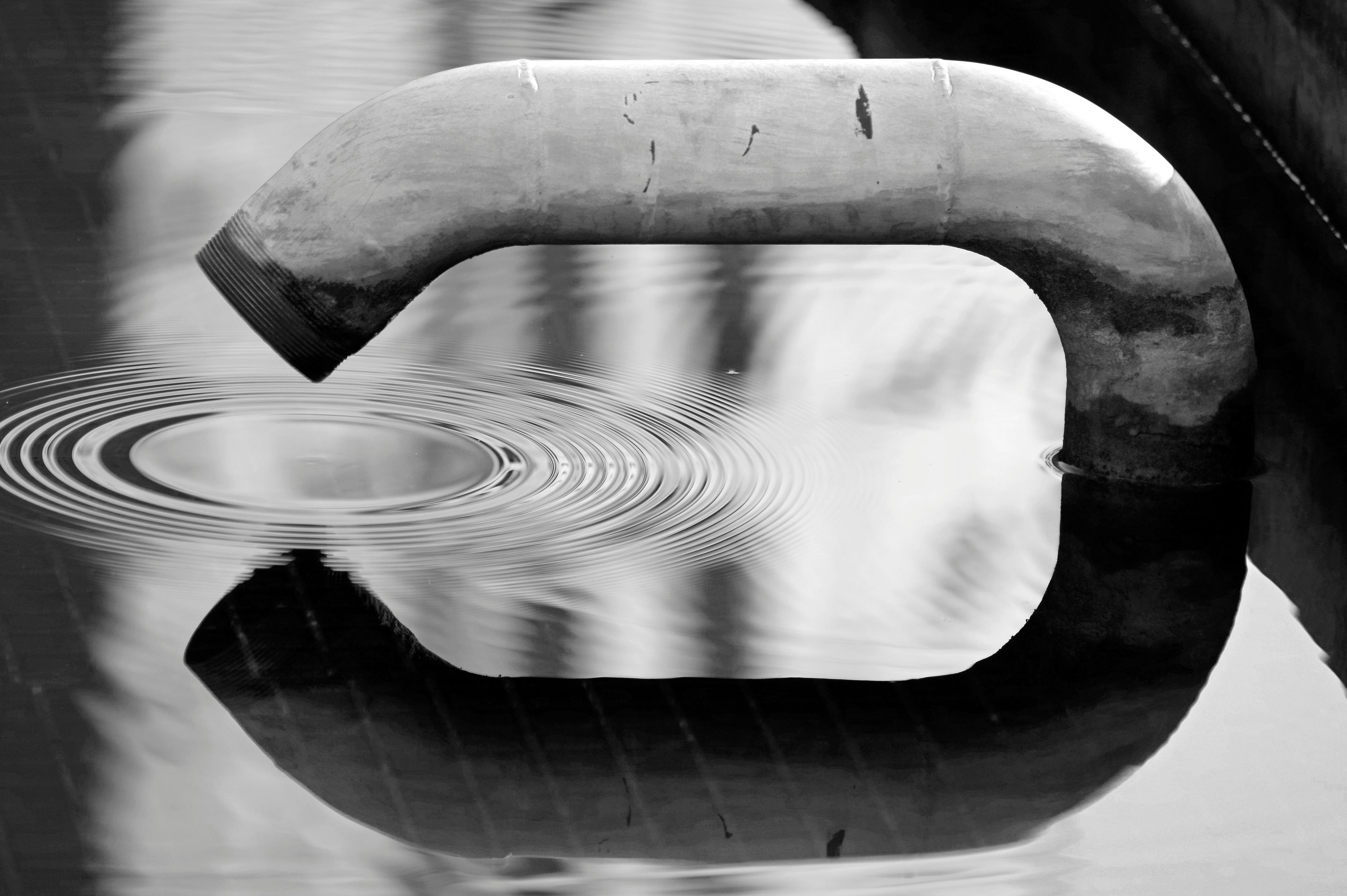 Ücretsiz Suyun üzerinde dalgalanmalar yaratan bir borunun siyah beyaz görüntüsü. Soyut bir yansıma sahnesi. Stok Fotoğraflar